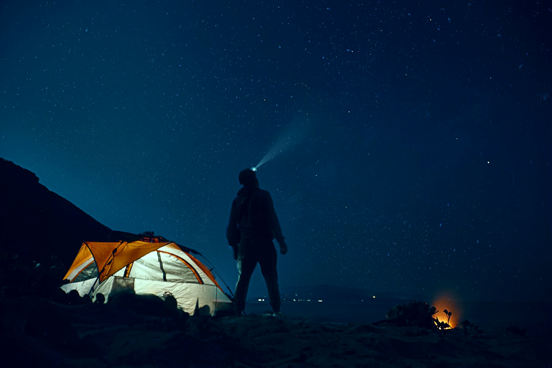 homme debout à côté d'une tente de camping portant une lampe frontale pendant la nuit